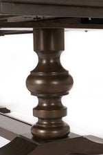 A close-up of a dark brown turned wood table leg with a fluted, bulbous design