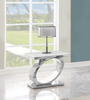 Modern white marble end table with chrome oval base and silver lamp in living room by window.