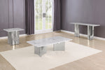 A modern three-piece table set featuring a rectangular coffee table, a smaller side table, and a long console table, all with white marble-look tops and polished silver bases, arranged on a cream rug in a room with gray walls and wood floors.