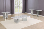 A modern three-piece table set featuring a rectangular coffee table, a smaller side table, and a long console table, all with white marble-look tops and polished silver bases, arranged on a cream rug in a room with gray walls and wood floors.