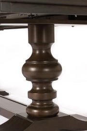 A close-up of a dark brown turned wood table leg with a fluted, bulbous design