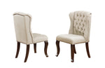 Upholstered dining chairs in light beige fabric with tufted buttons, nailhead trim, and dark brown wooden legs.